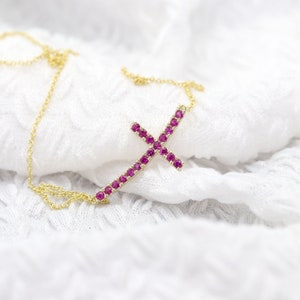 May include: A gold chain necklace with a pink ruby cross pendant. The cross is made of small pink rubies set in gold.