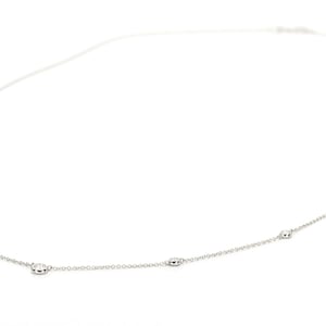 May include: A delicate silver necklace with several oval-shaped embellishments evenly spaced along the chain. The necklace is displayed against a white background, highlighting its minimalist design and elegant simplicity. The chain is thin and the embellishments are small.