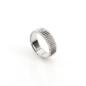 Puede incluir: Un anillo de plata con un dise&ntilde;o texturizado y estriado. El anillo es simple y elegante.
