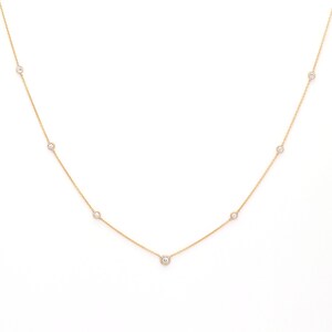 May include: A delicate gold necklace featuring several small, round, clear gemstones evenly spaced along the chain. The necklace is displayed against a bright white background, highlighting the jewelry's simple elegance.