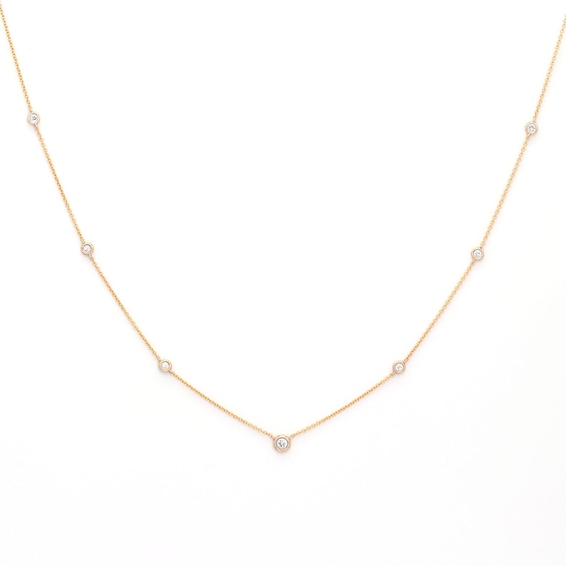 May include: A delicate gold necklace featuring several small, round, clear gemstones evenly spaced along the chain. The necklace is displayed against a bright white background, highlighting the jewelry's simple elegance.