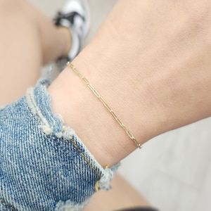 May include: A gold chain bracelet with a delicate, linked design. The bracelet is worn on a person's wrist.