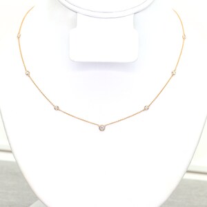 May include: A delicate gold necklace featuring several small, round, clear gemstones evenly spaced along the chain. The necklace is displayed on a white jewelry stand, showcasing its simple elegance.