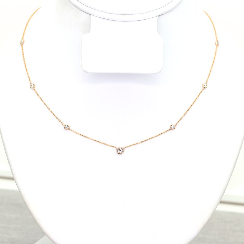 May include: A delicate gold necklace featuring several small, round, clear gemstones evenly spaced along the chain. The necklace is displayed on a white jewelry stand, showcasing its simple elegance.