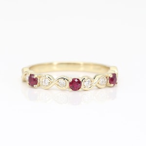May include: A gold band ring with a wavy design featuring alternating red rubies and white diamonds.