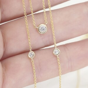 May include: A delicate gold necklace featuring three bezel-set diamonds. The diamonds are round and sparkle against the warm gold chain. The necklace is a simple yet elegant piece of jewelry.