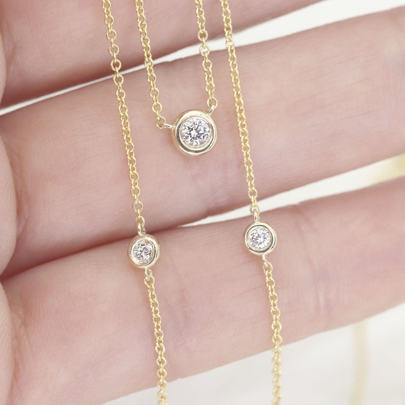May include: A delicate gold necklace featuring three bezel-set diamonds. The diamonds are round and sparkle against the warm gold chain. The necklace is a simple yet elegant piece of jewelry.