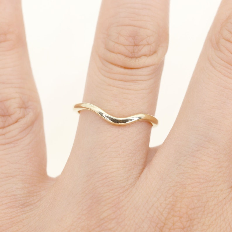 Op de afbeelding: Een eenvoudige gouden ring met een gebogen, golvend ontwerp. De ring wordt aan een vinger gedragen.