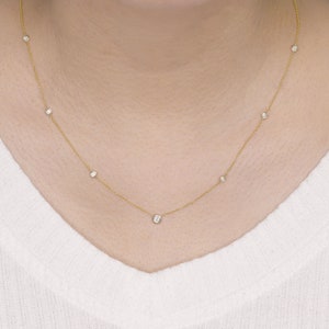 May include: A delicate gold necklace featuring several small, round, clear gemstones evenly spaced along the chain. The necklace is displayed against a white background, highlighting the jewelry's design and sparkle.