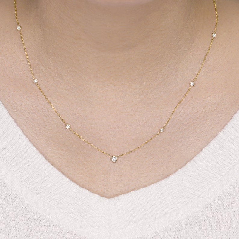 May include: A delicate gold necklace featuring several small, round, clear gemstones evenly spaced along the chain. The necklace is displayed against a white background, highlighting the jewelry's design and sparkle.