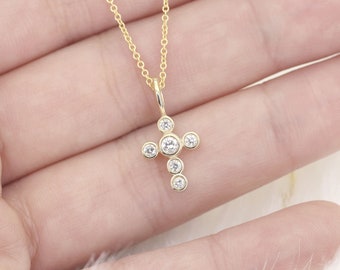 May include: A gold chain necklace with a small cross pendant featuring five clear round stones.
