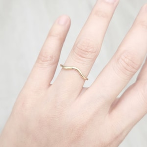 Op de afbeelding: Een ring in de vorm van een golf, gemaakt van goudkleurig metaal, gedragen aan een vinger.