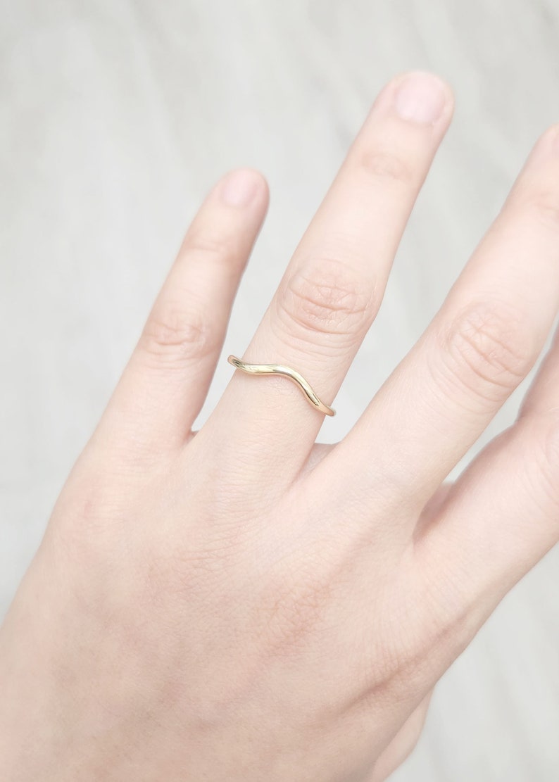 Op de afbeelding: Een ring in de vorm van een golf, gemaakt van goudkleurig metaal, gedragen aan een vinger.