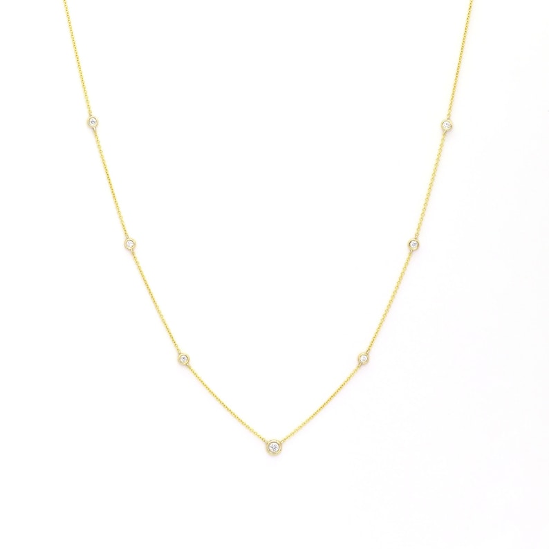 May include: A delicate gold necklace featuring several small, round, clear gemstones evenly spaced along the chain. The necklace is displayed against a white background, highlighting the jewelry's design and sparkle.