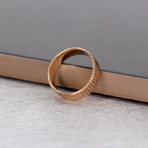 Puede incluir: Un anillo dorado con un dise&ntilde;o texturizado y estriado. El anillo est&aacute; sobre una superficie marr&oacute;n.