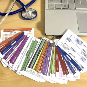 Peut inclure: Un ensemble de cartes de référence médicale multicolores déployées sur une surface, avec des étiquettes telles que Vital Signs, Pain Scale, Pediatric, Calculation, Stroke Scale, Apgar Score, Glasgow Coma Scale, EKG, Medication et Drug, près d'un ordinateur portable et d'un stéthoscope.