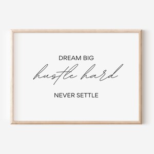 Può includere: Una citazione motivazionale in una cornice di legno. La citazione dice "Dream Big Hustle Hard Never Settle".