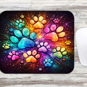 May include: A rectangular mousepad featuring a vibrant, colorful design of paw prints in a radial pattern. The paw prints are in shades of blue, green, yellow, orange, and pink against a dark background. A white computer mouse is on the right.