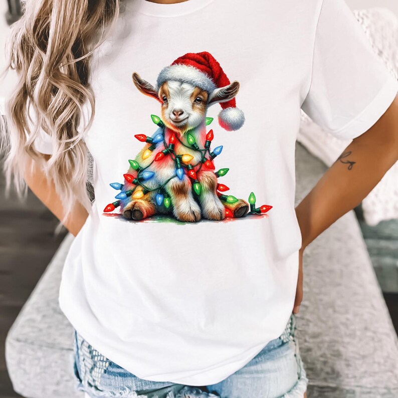 K&ouml;nnte beinhalten: Wei&szlig;es T-Shirt mit einem Cartoon-Bild einer Ziege, die einen Weihnachtsmann-Hut tr&auml;gt und in bunte Weihnachtslichter gewickelt ist.