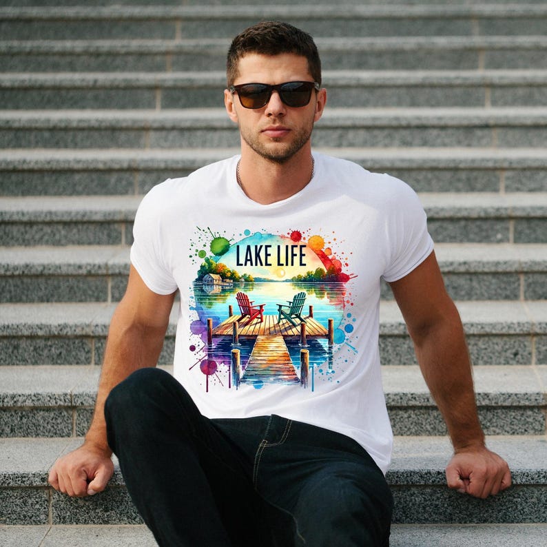 May include: White t-shirt with a watercolor design of a lake scene with two chairs on a dock. The text "LAKE LIFE" is printed on the shirt.