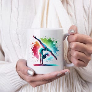 May include: White ceramic mug featuring a colourful illustration of a gymnast performing a handstand against a white background. The gymnast is depicted in a blue and green leotard with a splash of colour behind her.