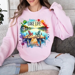 May include: Pink sweatshirt with a watercolor design of a lake scene with two chairs on a dock. The text "LAKE LIFE" is printed on the sweatshirt.