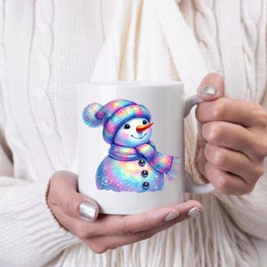 May include: White ceramic mug featuring a colourful snowman design. The snowman is wearing a blue and purple hat with a white pom-pom and a matching scarf. The snowman has a carrot nose and a happy expression.