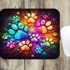 May include: A rectangular mousepad featuring a vibrant, colorful design of paw prints in a radial pattern. The paw prints are in shades of blue, green, yellow, orange, and pink, set against a dark background. A white computer mouse is on the right.