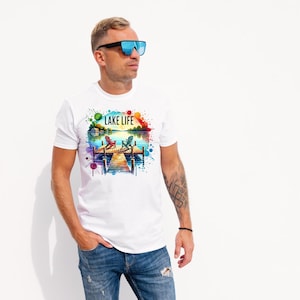 May include: White t-shirt with a colorful watercolor design of a lake scene with two chairs on a dock. The text "LAKE LIFE" is printed on the shirt.