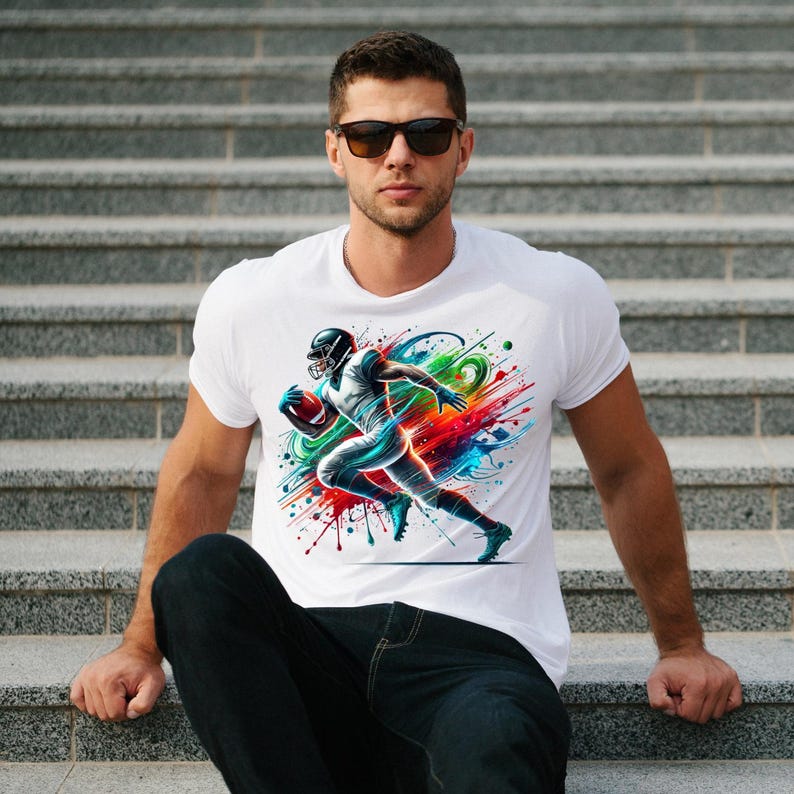 May include: White t-shirt with a colorful graphic of a football player running with the ball. The graphic has splashes of blue, red, green, and yellow paint.
