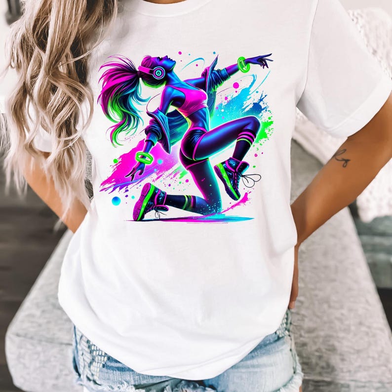 K&ouml;nnte beinhalten: Wei&szlig;es T-Shirt mit einem bunten Grafikdruck einer tanzenden Frau. Die Frau tr&auml;gt Kopfh&ouml;rer und eine Jacke. Die Grafik ist von bunten Farbstichen umgeben.