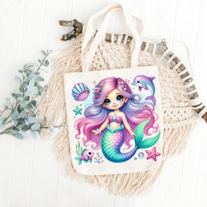 May include: A white canvas tote bag featuring a colorful illustration of a mermaid with purple and pink hair, a teal tail, and a seashell bra. A dolphin, starfish, and fish are also depicted. The bag has cream-colored handles.