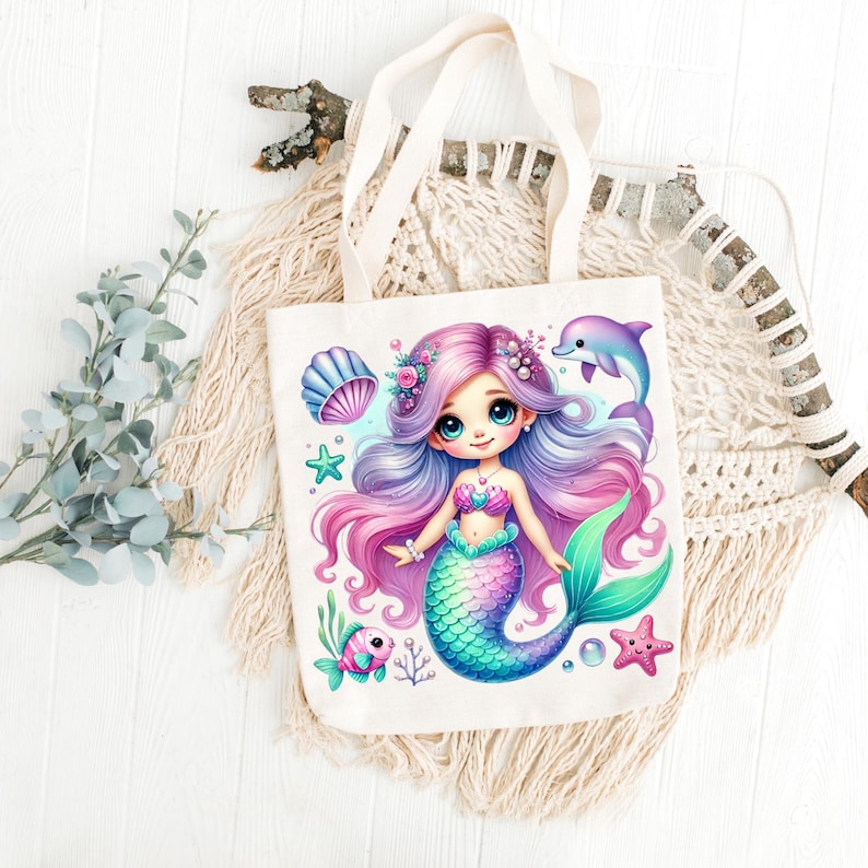 May include: A white canvas tote bag featuring a colorful illustration of a mermaid with purple and pink hair, a teal tail, and a seashell bra. A dolphin, starfish, and fish are also depicted. The bag has cream-colored handles.