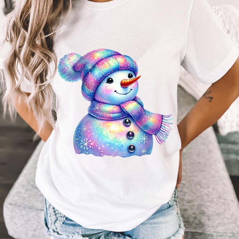 May include: White t-shirt featuring a colourful cartoon snowman wearing a rainbow striped hat and scarf. The snowman has a carrot nose and black eyes.