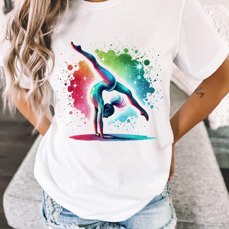 May include: White t-shirt featuring a colourful graphic of a gymnast performing a back handspring against a galaxy-like background.