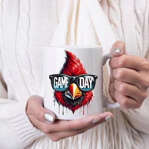 May include: White ceramic coffee mug featuring a red cardinal wearing sunglasses and the text "GAME DAY".