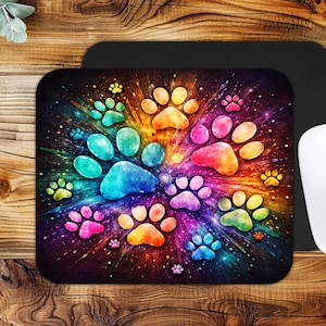 May include: A colorful mousepad featuring a vibrant design of paw prints in a rainbow of colors. The paw prints are arranged in a burst pattern against a dark background with a starry effect. A white computer mouse is on the right.