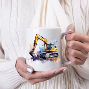 May include: White ceramic mug with a watercolour illustration of a yellow excavator. The design includes blue, brown, and yellow paint splashes. The excavator has a detailed bucket and tracks. The mug is held by a person wearing a white sweater.