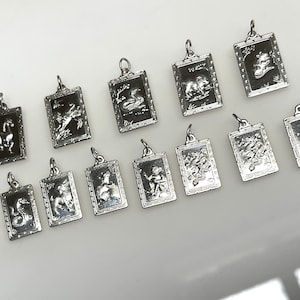 May include: Twelve silver charms, each featuring a different Chinese zodiac animal, are displayed on a white surface. The charms are rectangular in shape and have a detailed design.