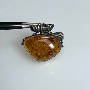 May include: A silver pendant with a large amber stone set in a delicate wire design. The amber is a warm, honey color with inclusions.