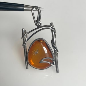 May include: A silver pendant with a large amber stone set in a twisted wire frame.