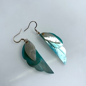May include: A pair of blue and white shell earrings with a gold accent. The earrings are shaped like wings.