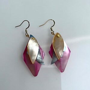May include: A pair of pink and white shell earrings with gold hooks. The earrings are shaped like diamonds and have a layered design.
