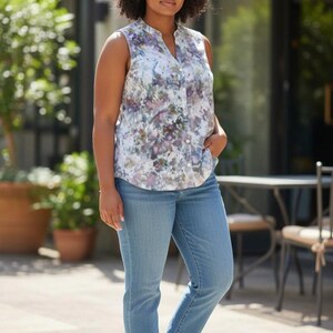 May include: Sleeveless floral print blouse with a mandarin collar and button-down front. The blouse is paired with light blue denim jeans. The floral pattern features shades of purple, white, and green.