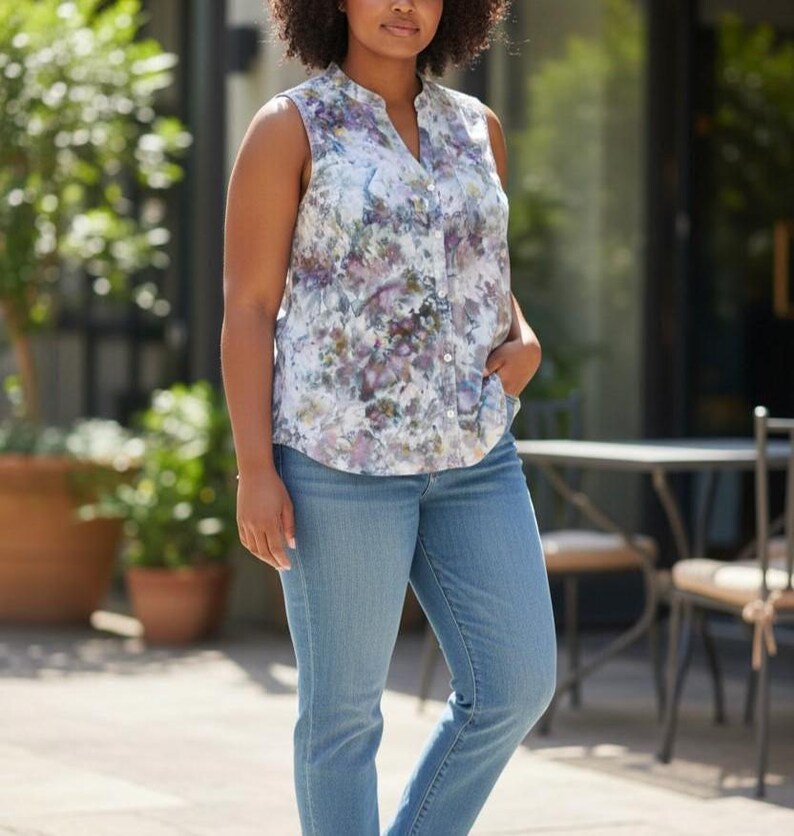 May include: Sleeveless floral print blouse with a mandarin collar and button-down front. The blouse is paired with light blue denim jeans. The floral pattern features shades of purple, white, and green.