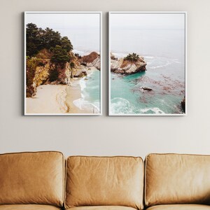 May include: Two framed photographs of a rocky coastline with turquoise water and a sandy beach. The photos are hung on a white wall above a brown leather couch.