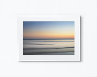 May include: A framed photograph of a blurred seascape at sunset. The sky is a gradient of blue, pink, and orange, and the water is a soft, muted blue. The horizon is a thin line of white.