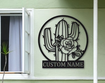 May include: Black metal wall art featuring a cactus with a flower and a custom name plate. The art is mounted on a light green wall with a house number "2503" visible.