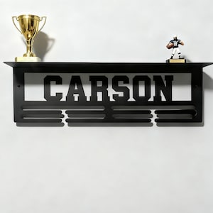 May include: Black metal shelf with the name "CARSON" cut out. A gold trophy and a football player figurine are displayed on the shelf. The shelf has three horizontal slots below the name.