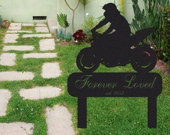 Puede incluir: Silueta negra de metal de una persona conduciendo una motocicleta con las palabras "Forever Loved est. 2023" en un letrero debajo. La silueta está frente a un césped verde y un camino de piedra que conduce a una casa.